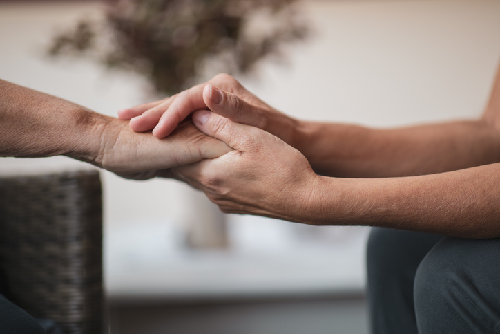 Two people are sitting down, and one person is holding and caressing another hand. The picture is a close-up of the hands.