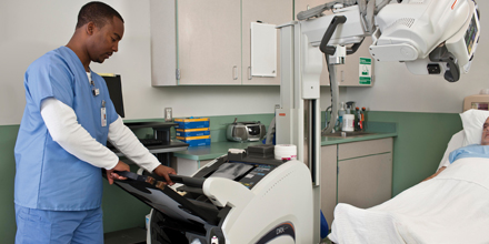 Photo of a man in scrubs preforming an X-ray on a patient. 